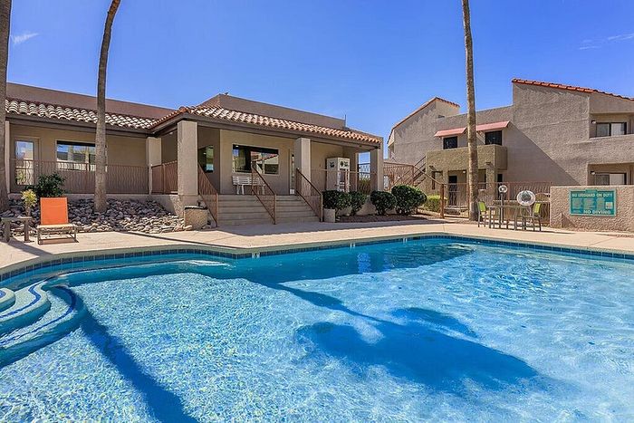 Inviting outdoor pool area with a modern apartment complex, surrounded by lush landscaping and sun-soaked seating.