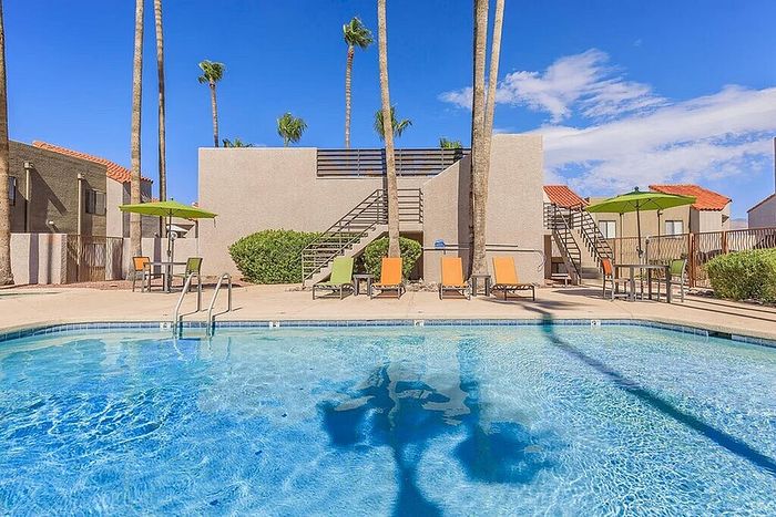 Luxurious swimming pool area with sun loungers and umbrellas surrounded by modern apartment buildings under a clear blue sky.