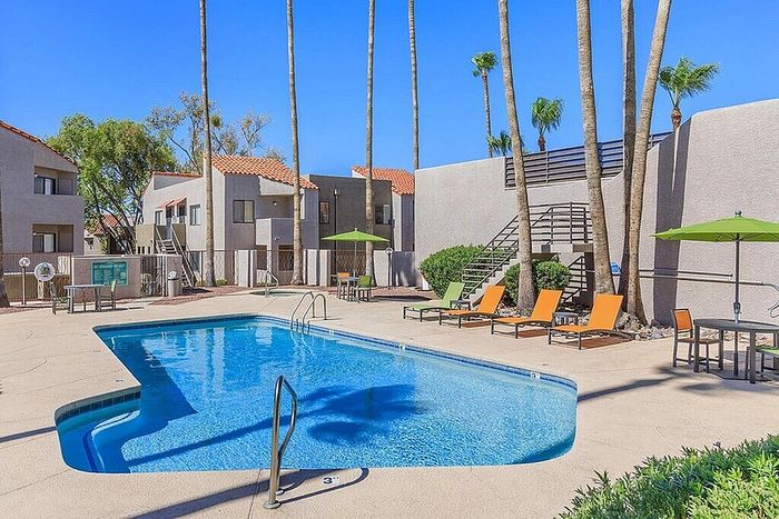Inviting pool area with sun loungers and umbrellas, surrounded by modern apartments and tall palm trees, ideal for relaxation and leisure.