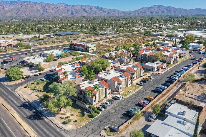 Scenic aerial view of a vibrant apartment complex with red-tiled roofs and ample parking, set against a backdrop of majestic mountains.