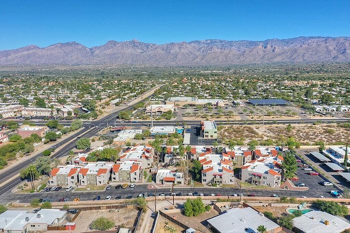 Breathtaking aerial view of a vibrant residential community with charming red-roofed houses, set against majestic mountain scenery and clear blue skies.