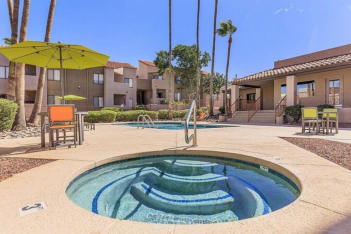 Inviting residential complex with modern amenities featuring a sparkling spa and pool area surrounded by vibrant greenery and seating under lush umbrellas.
