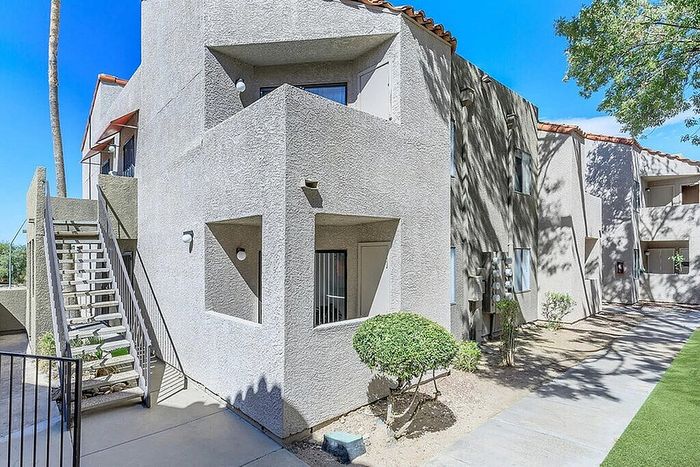 Modern apartment exterior with clean architectural lines, private balconies, and a vibrant landscaped walkway.
