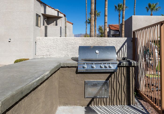 Modern outdoor grilling area with built-in barbecue, surrounded by palm trees and elegant architecture.