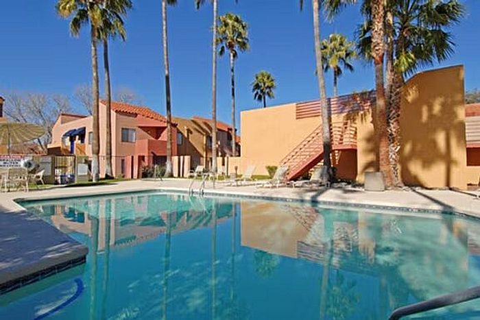 Vibrant apartment complex with a refreshing swimming pool surrounded by tall palm trees under a clear blue sky.