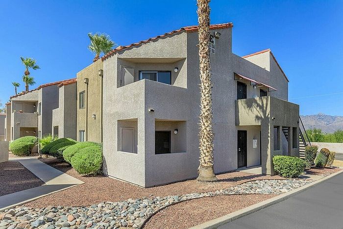Modern apartment complex with charming balconies, surrounded by desert landscaping and mountain views under a clear blue sky.