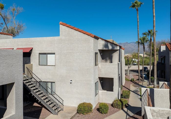 Charming apartment exterior with a sunny balcony, surrounded by palm trees and set against a stunning mountain backdrop.