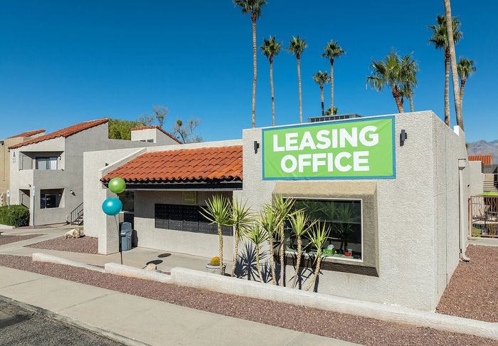 Inviting leasing office with a vibrant green sign and desert landscaping, surrounded by palm trees and clear blue skies.