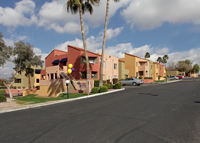 Vibrant apartment complex with colorful facades, lush greenery, and palm trees under a bright blue sky.