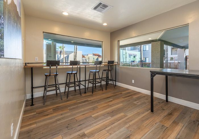 Bright communal space with stylish wooden flooring, featuring a high counter with barstools and large windows offering scenic outdoor views.