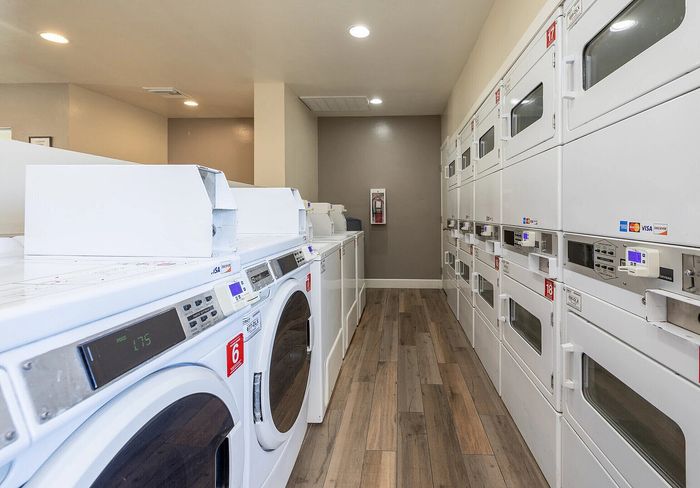 Modern laundry room with sleek white washers and dryers, featuring contemporary wood flooring and ample lighting.