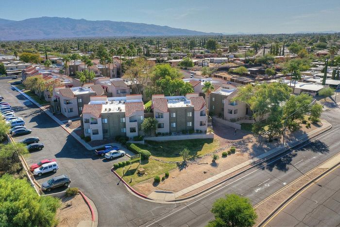 Charming apartment complex with red-tiled roofs surrounded by lush greenery and ample parking, set against a picturesque mountain backdrop.
