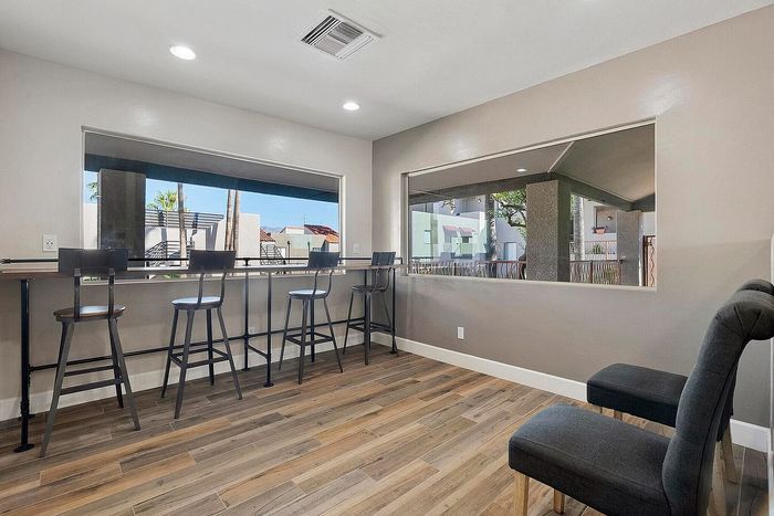 Bright and modern apartment nook with tall windows showcasing an outdoor view, featuring sleek bar seating and stylish grey chairs on elegant wooden flooring.
