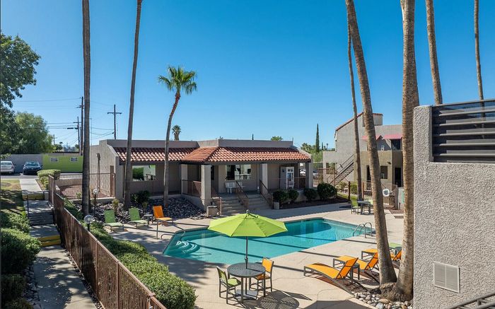 Inviting apartment complex featuring a sparkling pool, vibrant lounge chairs, and tropical landscaping under a clear blue sky.