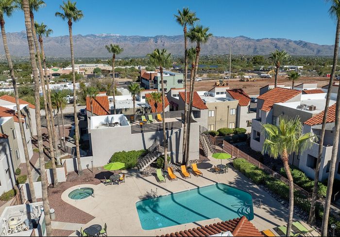 Vibrant apartment complex with a refreshing pool, lush palm trees, and scenic mountain views.