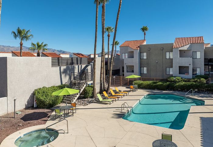 Bright apartment complex courtyard with a refreshing pool, cozy hot tub, sun loungers, and vibrant palm trees under a clear blue sky.