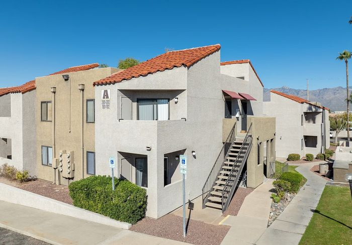 Charming apartment complex with modern architecture, featuring unique angled roofs and exterior staircases, set against a clear blue sky and mountain backdrop.