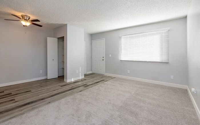 Bright and spacious room with modern ceiling fan and a blend of carpet and wood flooring, offering abundant natural light through a large window.