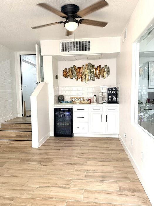 Bright modern kitchenette with a wine cooler, elegant wooden flooring, stylish wall art, and a ceiling fan.