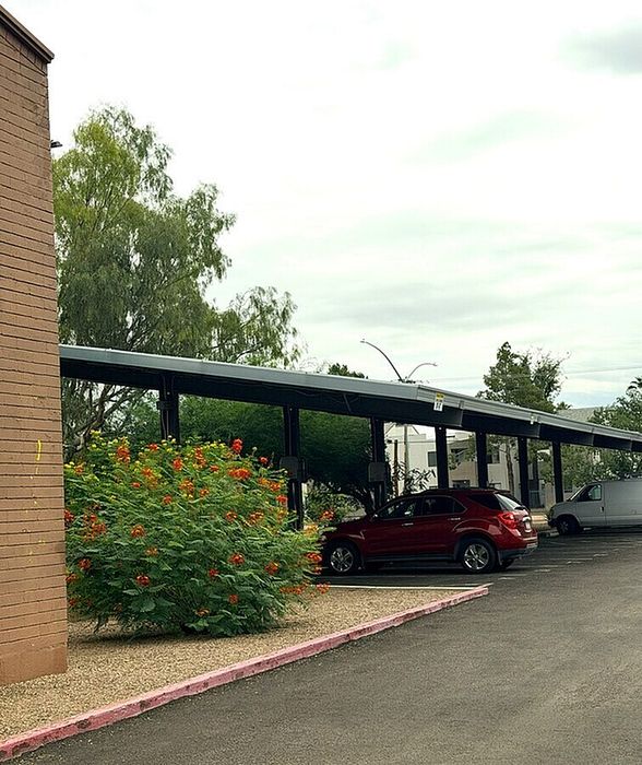 Charming apartment complex with a vibrant garden and covered parking area, featuring lush greenery and convenient vehicle spaces.