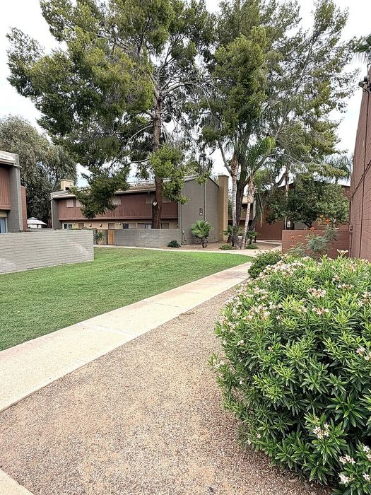 Tranquil residential area with lush greenery, paved pathways, and charming brick townhouses under tall trees.