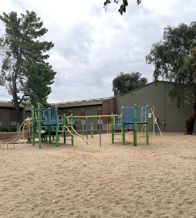 Inviting playground area with colorful climbing structures and slides, surrounded by a sandy play zone and lush trees, perfect for family fun.