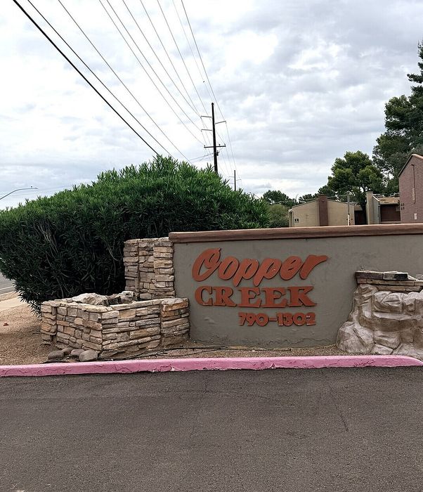 Inviting entrance to Copper Creek community with rustic stone sign and lush greenery, exuding a welcoming atmosphere.