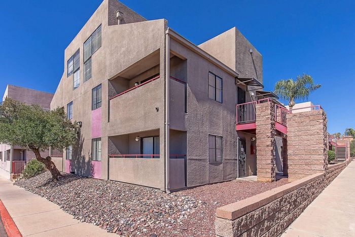 Charming apartment complex with modern design, featuring spacious balconies and surrounded by beautiful landscaping under a clear blue sky.