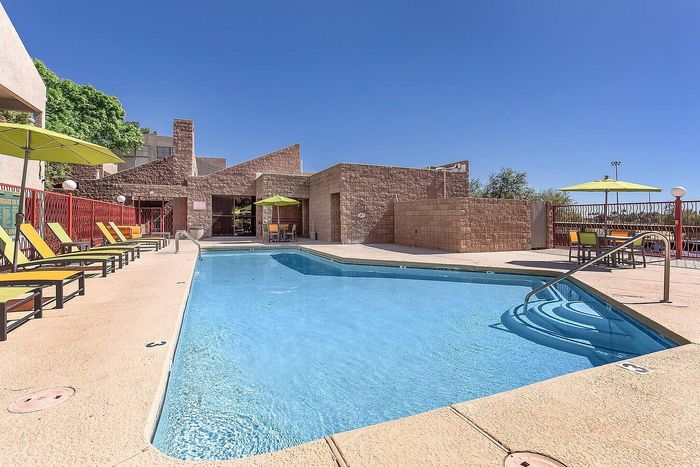 Inviting outdoor pool area with stylish sun loungers and shaded tables under vibrant umbrellas, perfect for relaxation.