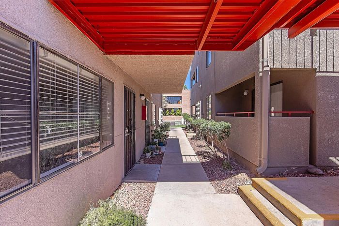 Charming apartment entrance with vibrant red awning and lush greenery lining the walkway.