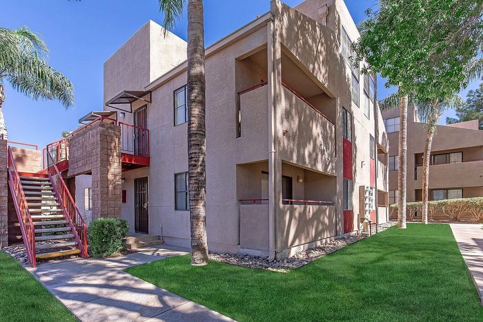 Charming apartment building with palm trees and lush green lawn, featuring modern architecture and sunny exterior walkways.