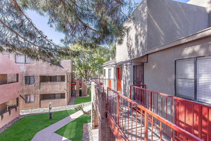 Charming apartment exterior with bright red accents, lush green landscaping, and inviting walkways under a sunny sky.