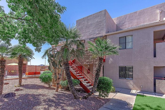 Inviting apartment exterior with vibrant red staircase and lush palm landscaping under a clear blue sky.