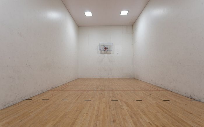 Spacious indoor basketball court with polished wooden flooring and bright lighting, perfect for recreational sports.