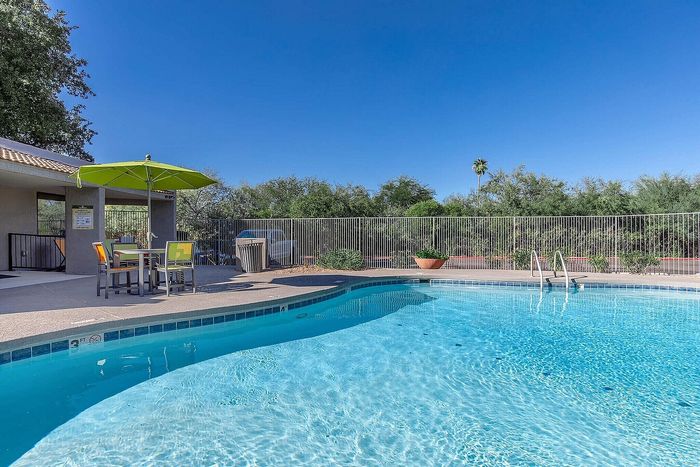 Inviting outdoor pool area with crystal-clear water, complemented by vibrant poolside seating and a large green umbrella.