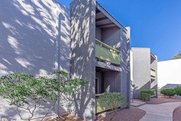 Charming apartment exterior with modern balconies and lush greenery under a bright blue sky.