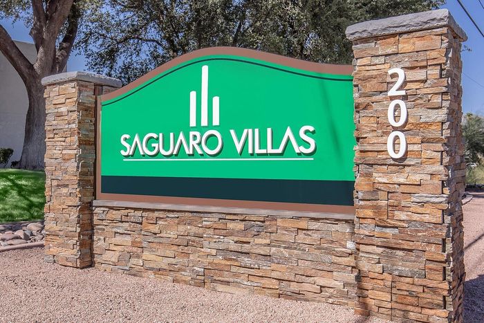 Inviting entrance to Saguaro Villas with a stylish stone sign and vibrant greenery, showcasing a welcoming community vibe.
