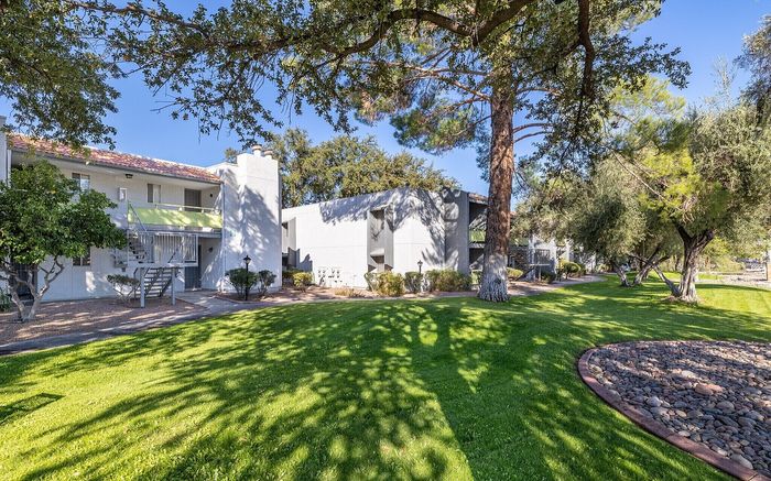 Charming apartment complex with lush green lawns, mature trees, and a peaceful courtyard setting.