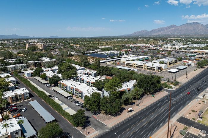 Vibrant aerial view of a modern apartment complex surrounded by lush greenery, with easy access to shopping and mountain views.