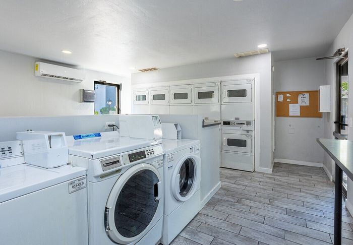 Modern and spacious laundry room equipped with multiple washers and dryers, featuring sleek tile flooring and ample natural light.