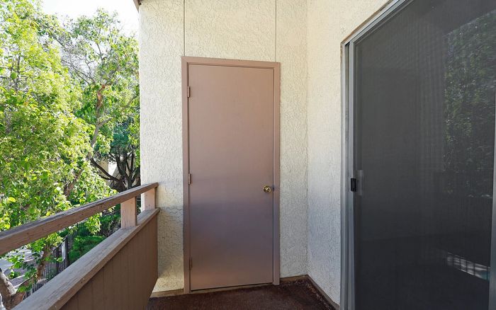 Charming balcony with lush green views, featuring a door and sliding glass entrance.