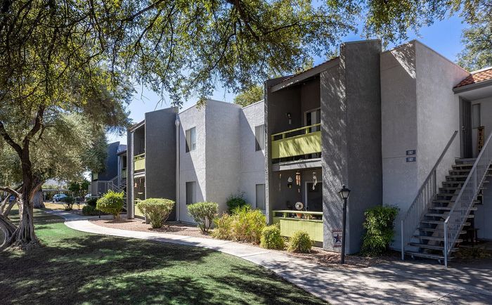 Charming apartment complex with lush greenery, shaded walkways, and stylish balconies in a serene setting.