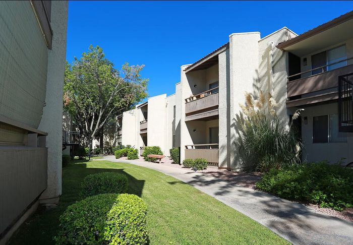 Charming apartment exterior with lush landscaping, manicured lawns, and a serene walkway under a clear blue sky.