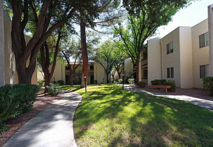 Charming apartment complex with lush green landscaping and inviting walking paths under mature trees.