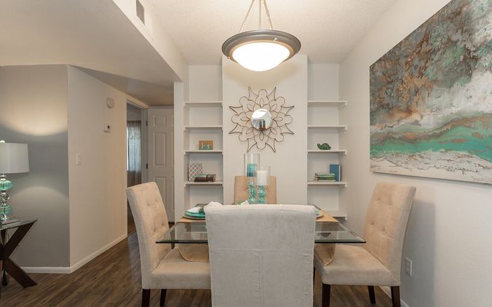 Elegant dining area with a glass-top table, plush beige chairs, contemporary artwork, and stylish built-in shelves, creating a welcoming and sophisticated atmosphere.