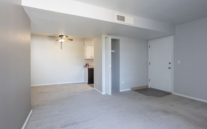 Bright and airy apartment interior with neutral tones, featuring plush carpet, ceiling fan, and a glimpse of the contemporary kitchen.