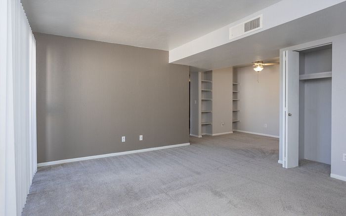 Spacious living area with plush carpet, built-in shelves, and a cozy ceiling fan for modern comfort.