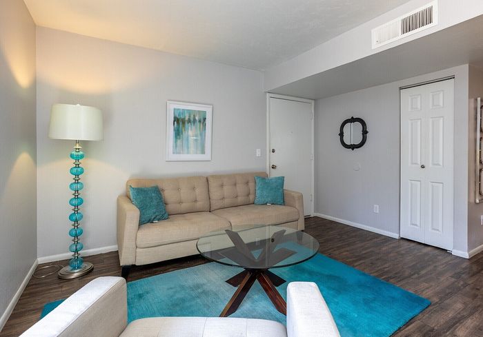 Elegant living room with a cozy beige sofa, vibrant teal accents, a modern glass coffee table, and stylish decor on rich wooden floors.