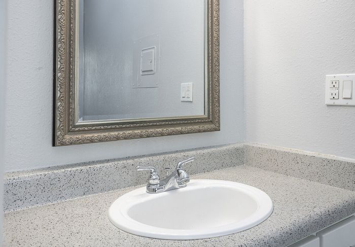 Elegant bathroom vanity featuring a sleek speckled countertop, polished silver faucet, and ornate framed mirror.