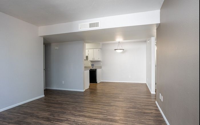 Modern open-concept living area with sleek wooden floors and contemporary lighting, leading to a bright kitchen space.